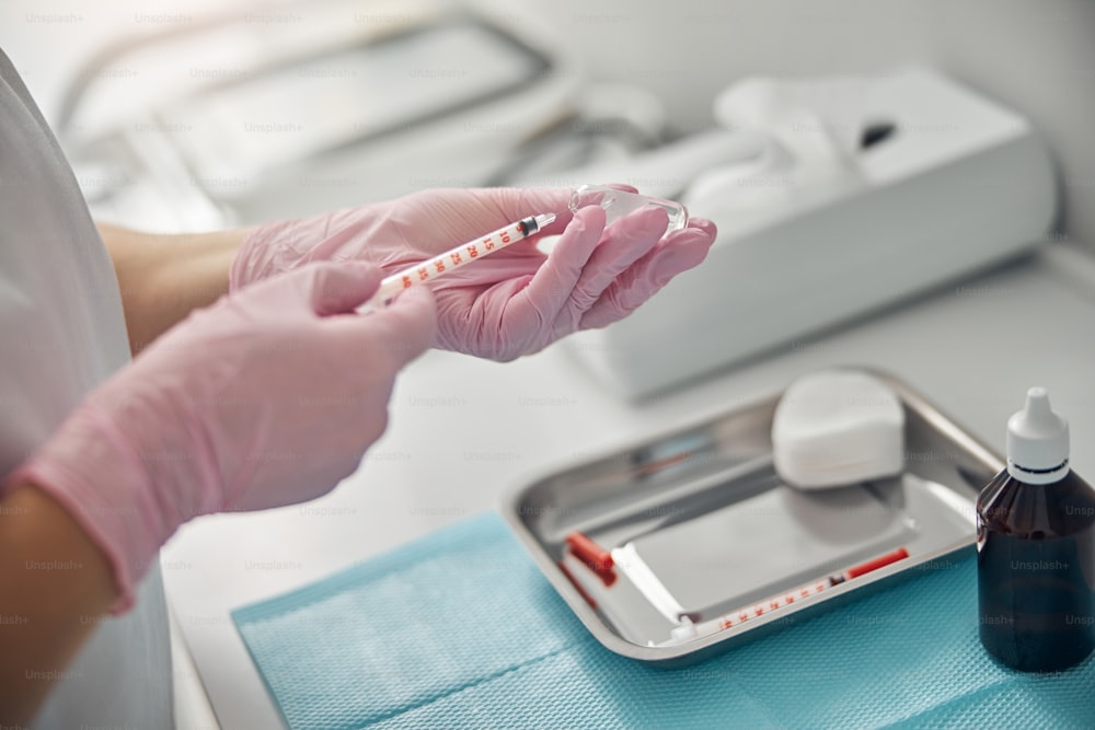 Nahaufnahme einer jungen Ärztin in sterilen Handschuhen, die Spritze mit Medikamenten füllt