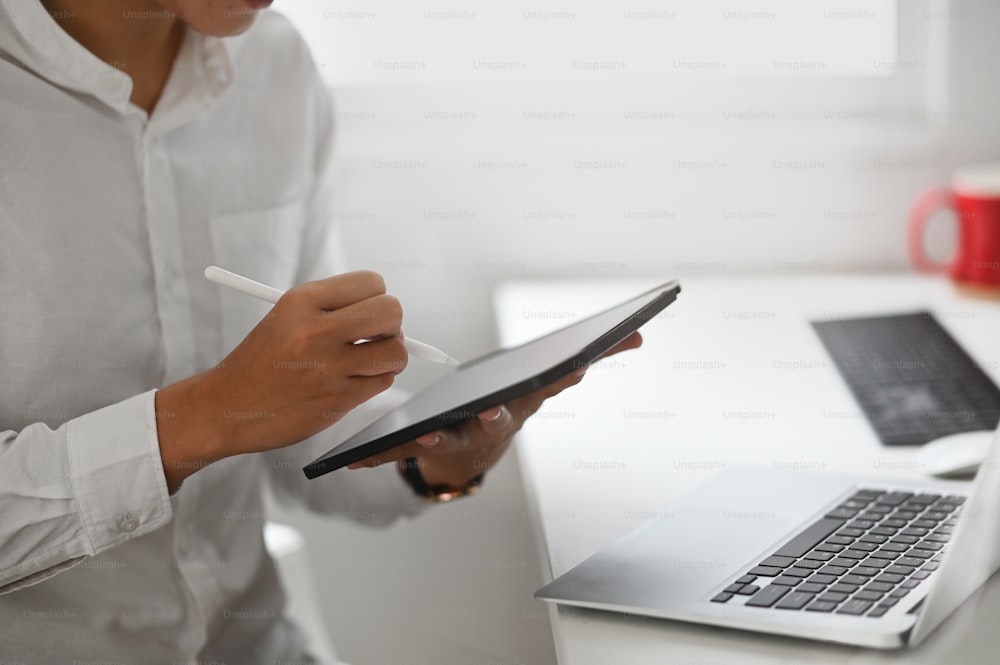 Homme créatif recadré travaillant avec une tablette numérique et un stylet au bureau à domicile.