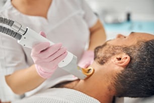 Female esthetician hands in sterile gloves removing unwanted hair from male neck with special laser device