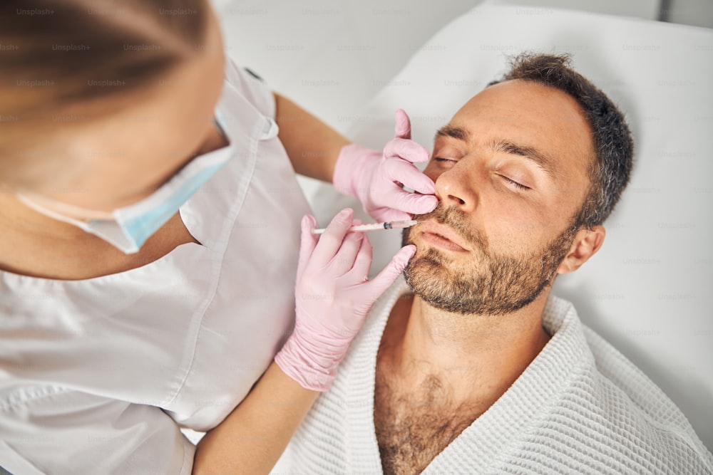 Femme médecin cosmétologue en gants stériles faisant l’injection dans le visage masculin