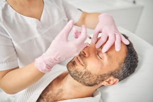 Close up de cosmetologista médico do sexo feminino em luvas estéreis fazendo injeção na testa masculina