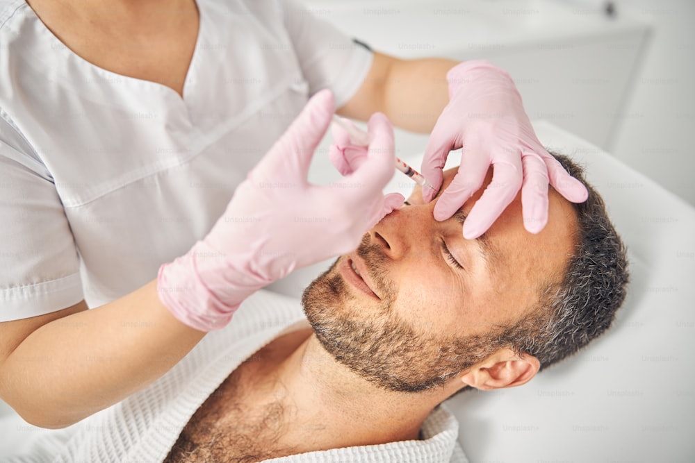 Nahaufnahme einer Ärztin in sterilen Handschuhen, die eine Injektion in die männliche Stirn vornehmen