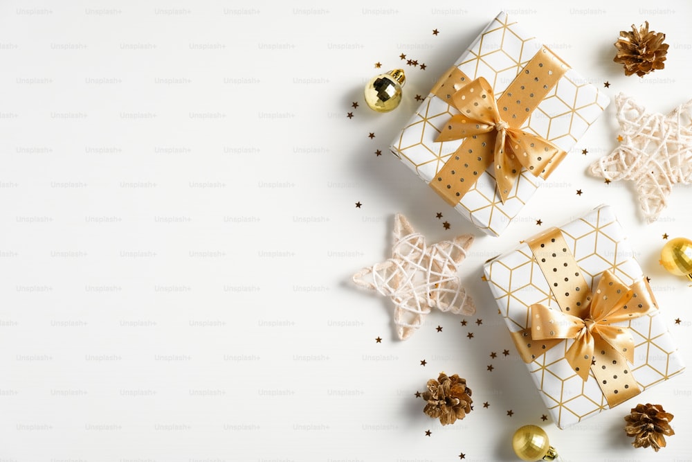 クリスマスフラットレイ構図。クリスマスの黄金の装飾、ギフトボックス、星、白い背景に紙吹雪。クリスマス、新年、冬休みのお祝いのコンセプト。グリーティングカード、はがきのモックアップ