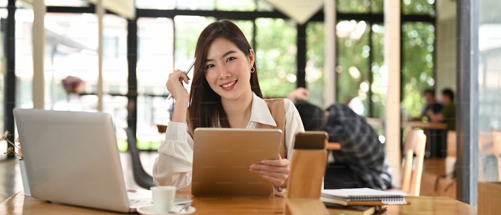 Businesswoman sitting in meeting room while working with tablet and laptop on wooden desk.