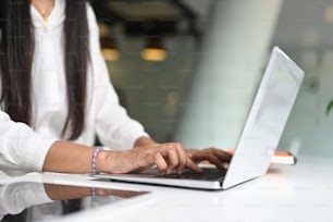 Cropped shot of businesswoman hands typing on laptop keyboard on white desk.