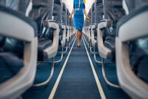 Cropped head portrait of female walking on the empty aisle in the dark blue color interior of commercial airplane
