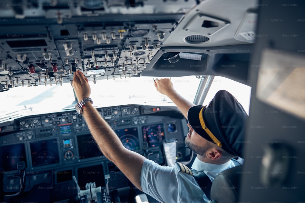 Ritratto di vista posteriore di maschio che indossa l'uniforme che preme i pulsanti nella cabina di pilotaggio durante il volo