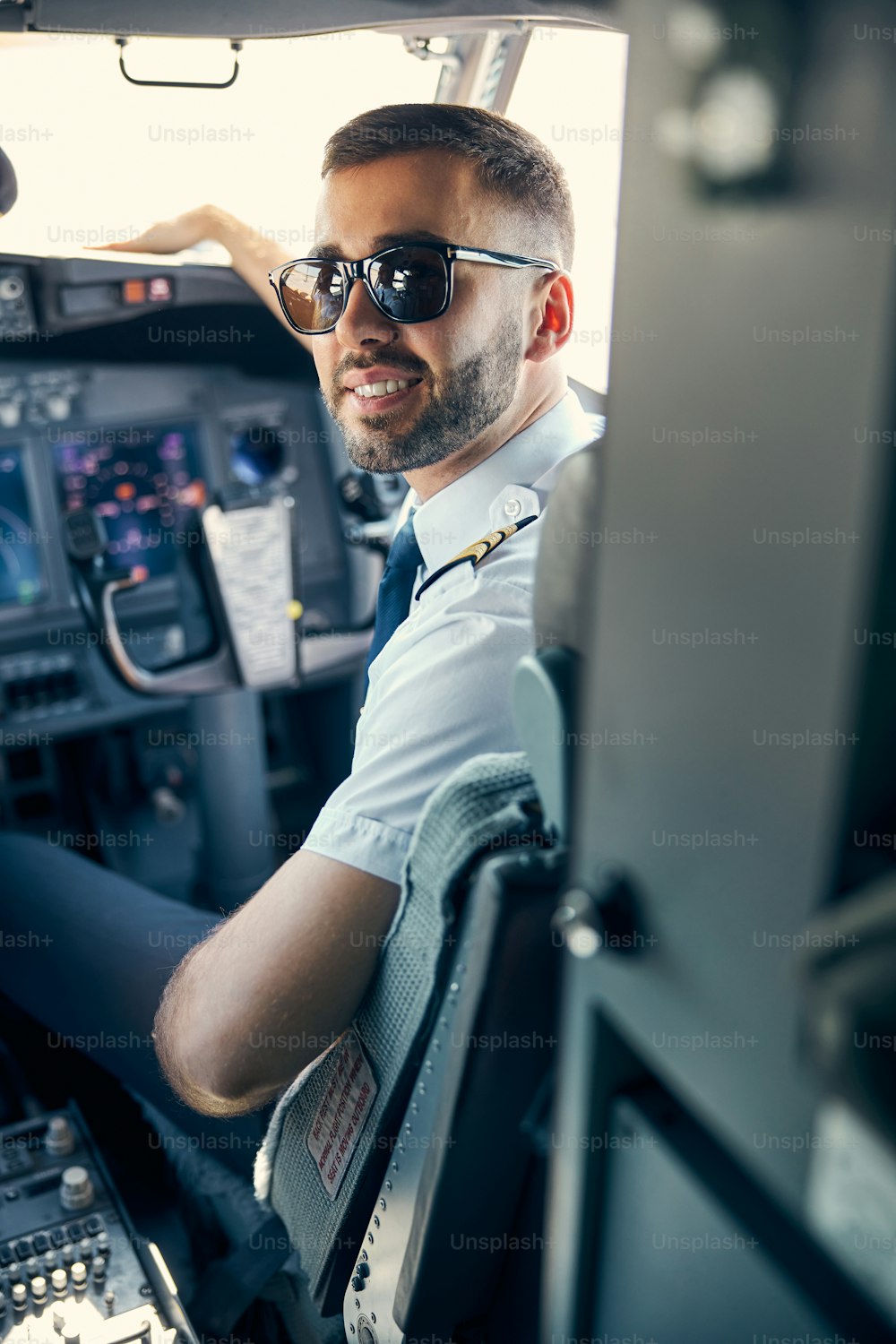Waist up portrait of stylish pilot sitting on the chair while posing at the photo camera