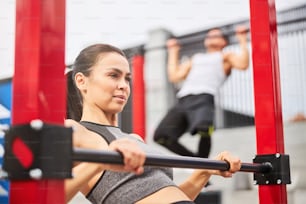 Pretty athletic female and strong male are exercising and doing pull ups on horizontal bars in open air