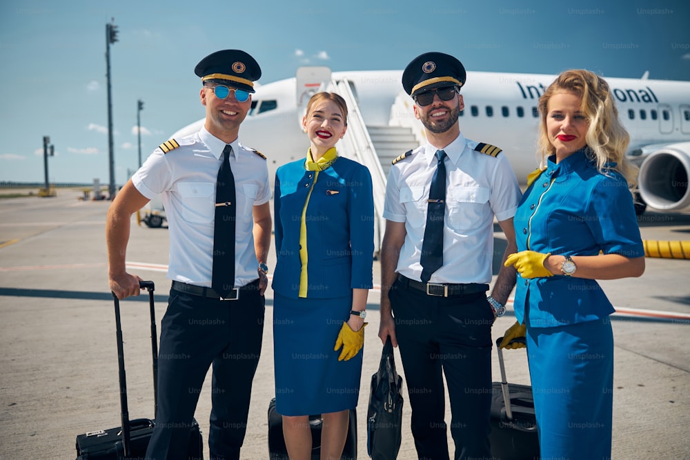 Handsome male pilots and beautiful female stewardesses looking at camera and smiling while holding travel suitcases