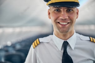 Cropped head portrait of confident pilot in white shirt standing in the salon of airplane