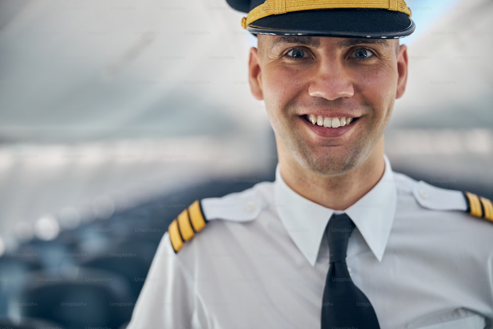 Retrato da cabeça cortada do piloto confiante na camisa branca em pé no salão do avião
