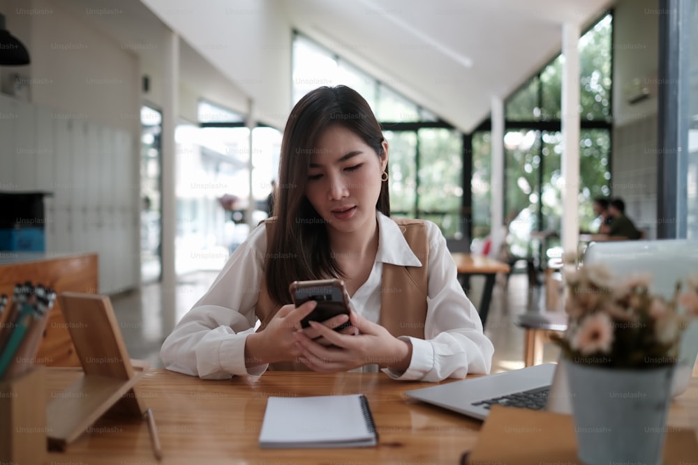 Young businesswoman using her smartphone with co working space background.