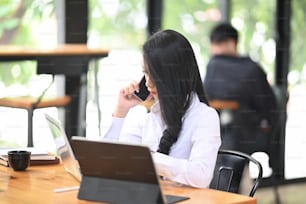 Young woman using a smartphone to calling someone while sitting in co working space.