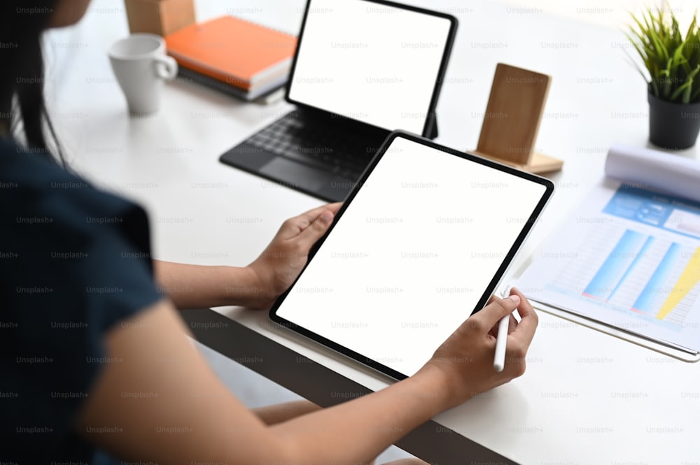 Abgeschnittene Aufnahme einer Frau mit Computer-Tablet und Analyse von Papierkram auf weißem Tisch.