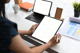 Cropped shot of woman using computer tablet and analyzing paperwork on white table.