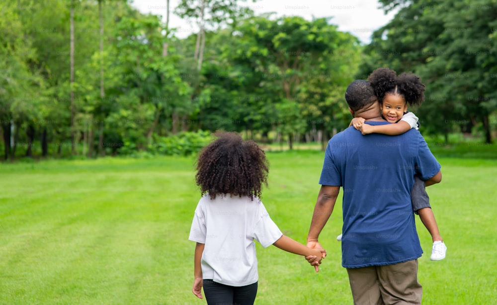 Felice padre africano con due figlie di razza mista che camminano insieme nel parco.