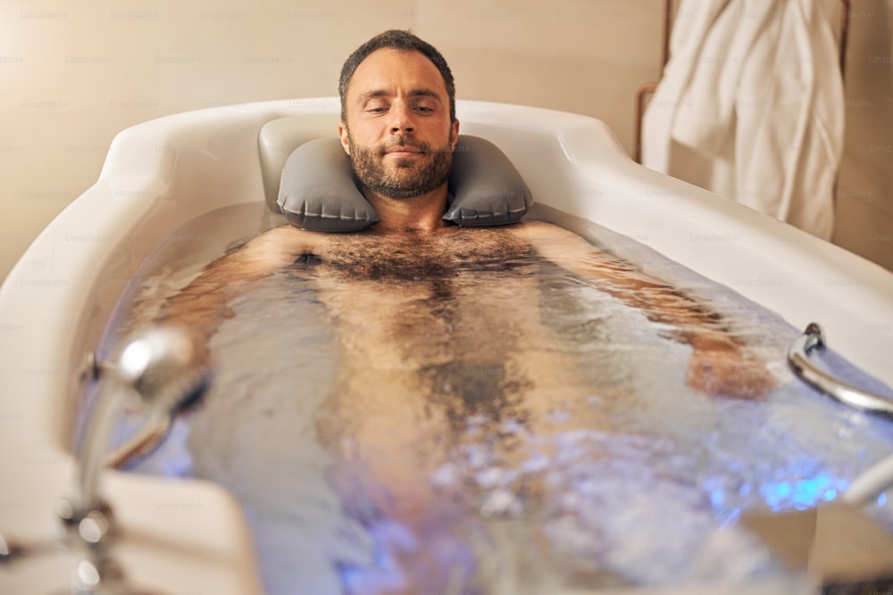 Bearded gentleman relaxing in bathtub while having hydrotherapy procedure