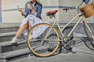 Close up portrait of retro vintage bicycle standing in front of charming good looking female with cup of coffee in the outdoors