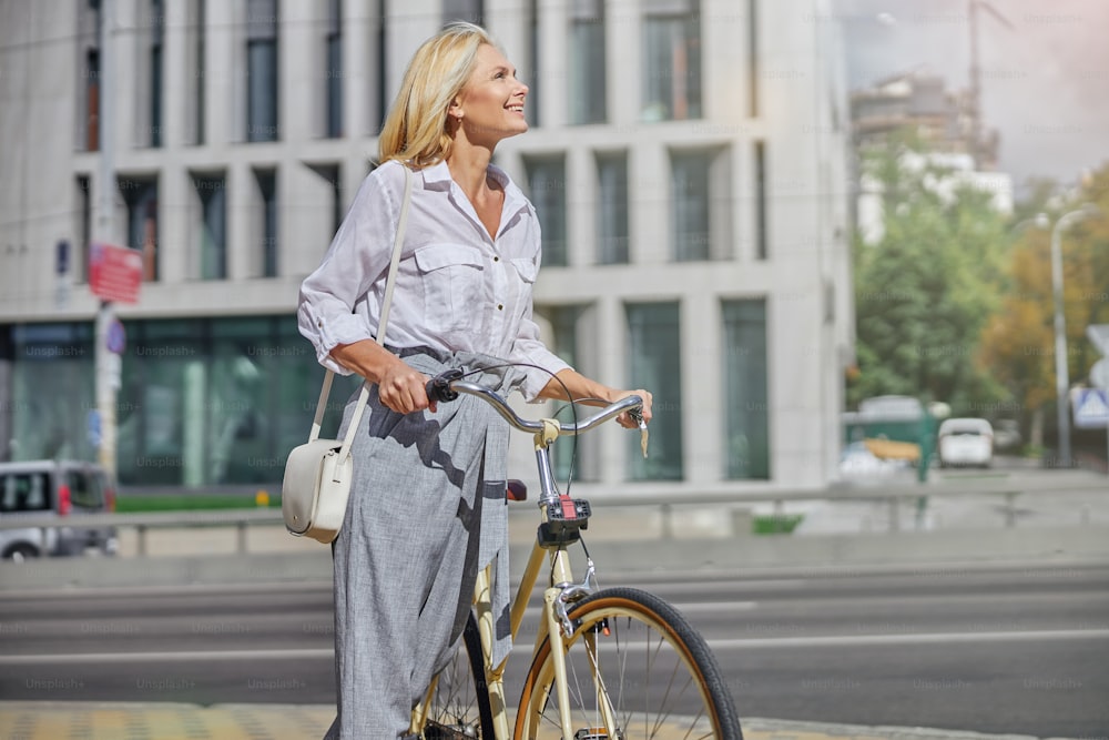 Close up portrait of businesswoman person in white going with her retro bicycle near modern buildings in city