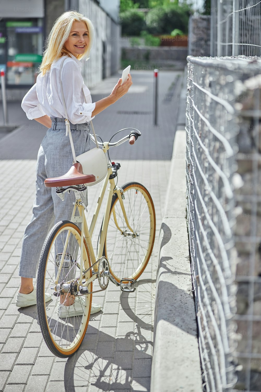 Portrait en pied d’une femme blonde souriante heureuse avec un vélo rétro jaune marchant dans la ville