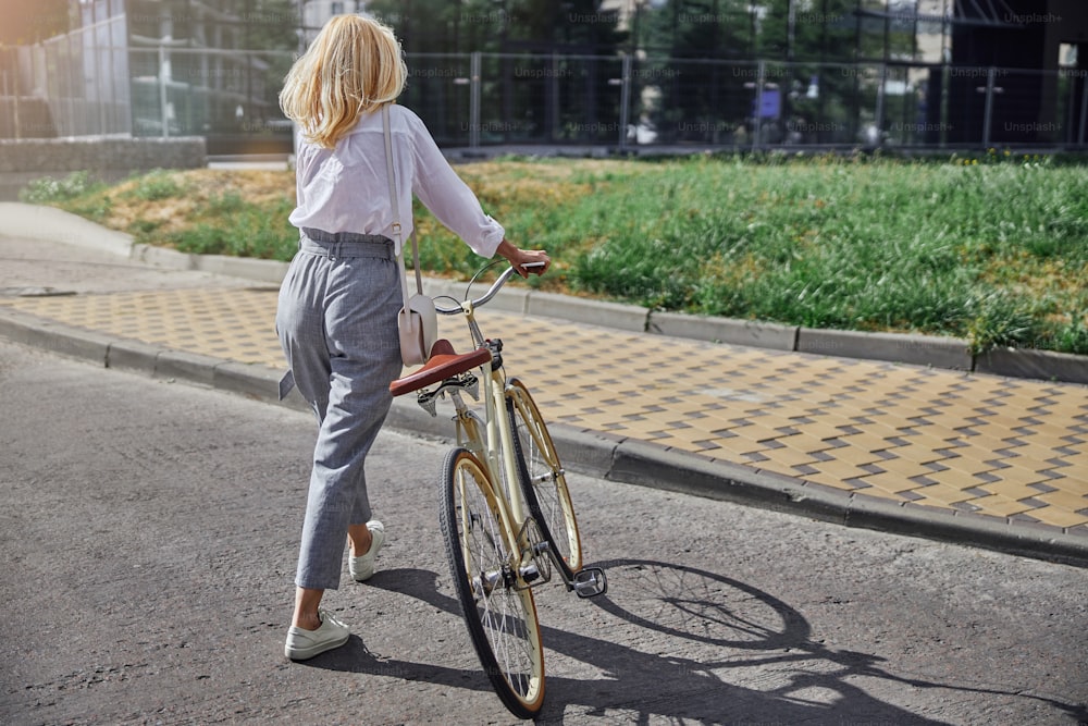 Back view portrait of woman tourist with retro city bicycle walking on the city street in the sun shine day