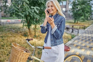 Retrato de vista lateral de mujer sonriente feliz con bicicleta retro hablando en teléfono inteligente en la calle de la ciudad