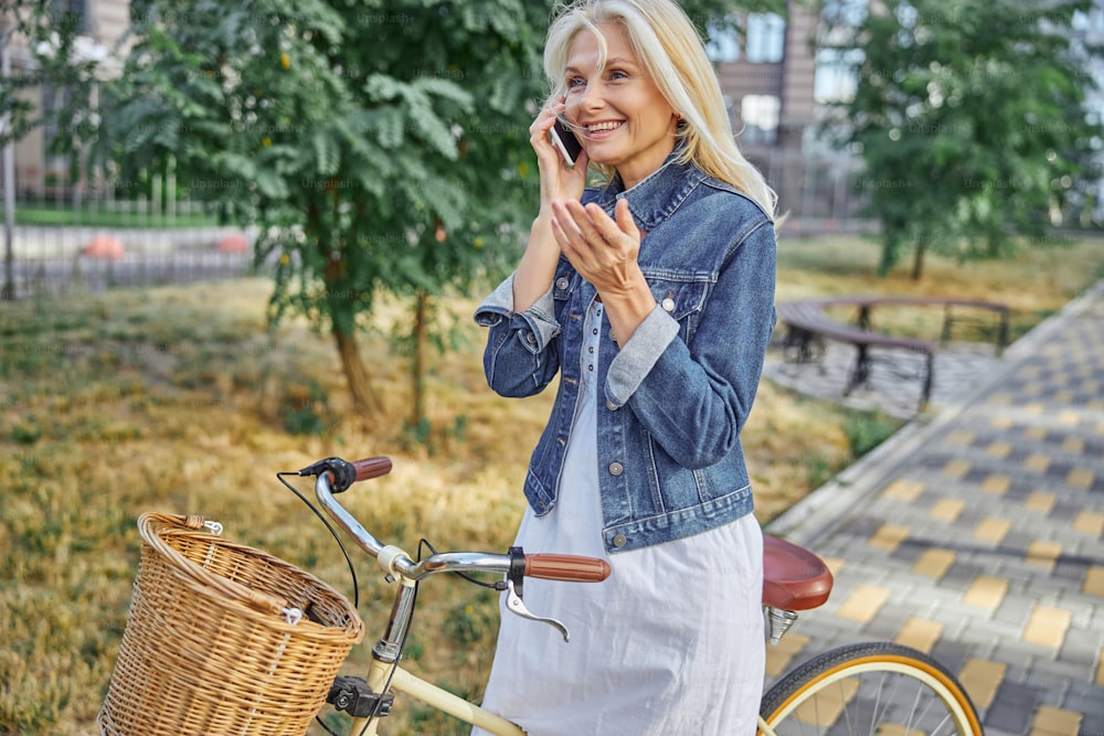 Side view portrait of happy smiling female with retro bike talking on smartphone in the city street