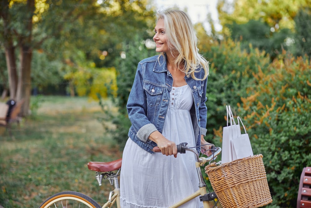 Side view portrait of happy smiling blonde Caucasian woman with retro bike relaxing in the city square