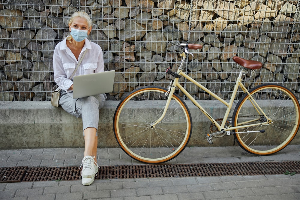 Retrato de cuerpo entero de mujer atractiva adulta en blusa blanca con bicicleta retro cerca de la pared de piedra en la ciudad