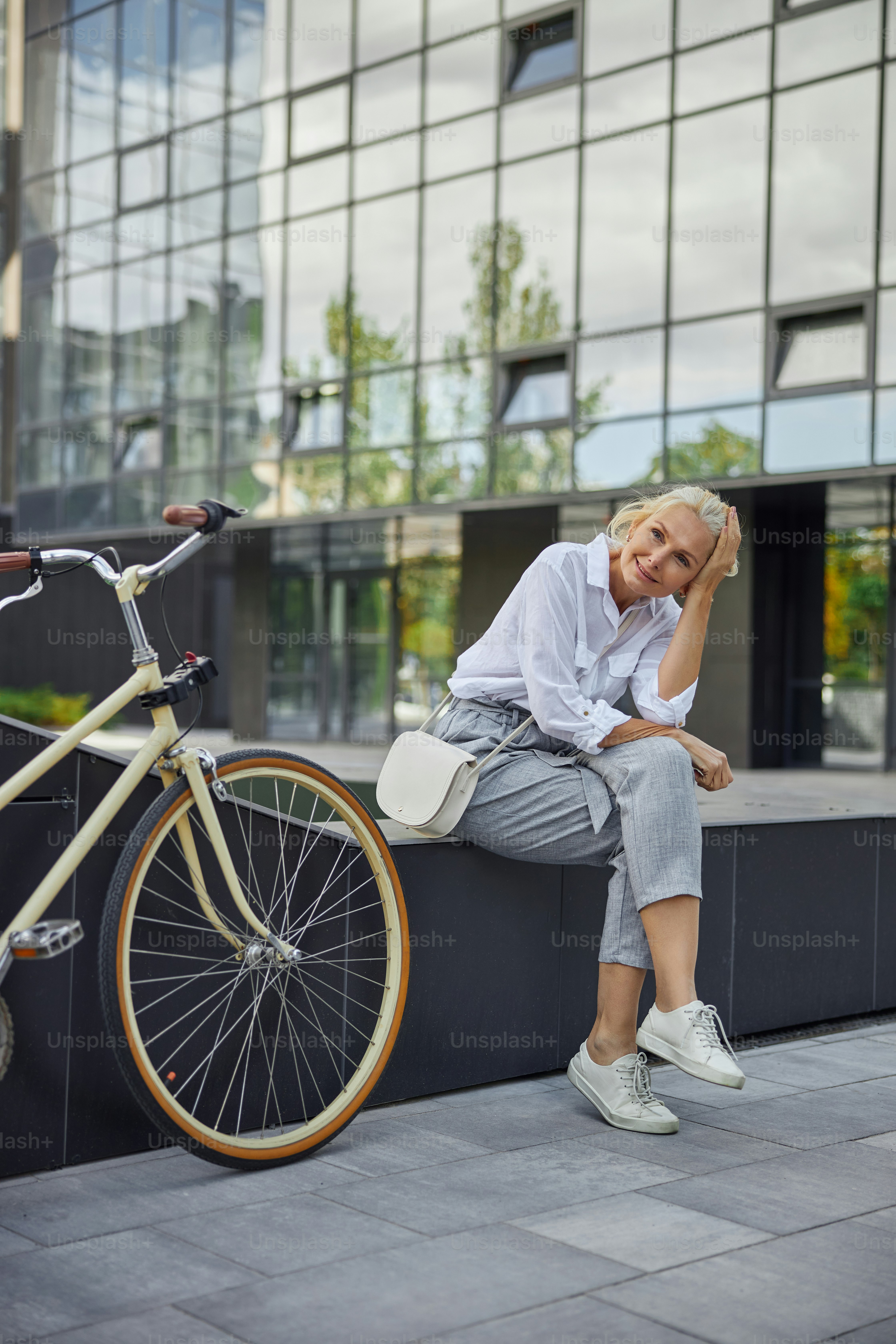 Full length portrait of happy Caucasian business lady sitting in front of modern business center while looking at the photo camera