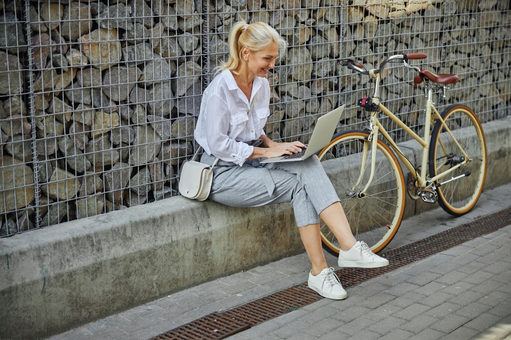 Retrato de cuerpo entero de la vista lateral de la mujer feliz sonriendo enviando mensajes de texto a su socio de negocios mientras pasa tiempo al aire libre