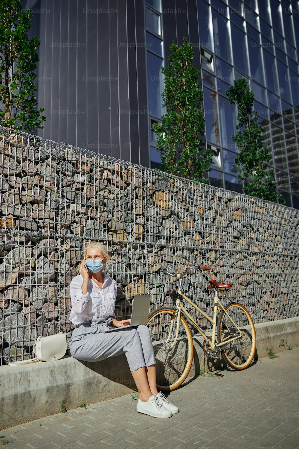 Retrato de corpo inteiro da mulher de negócios com bicicleta retro perto dela trabalhando no laptop no lugar urbano da cidade