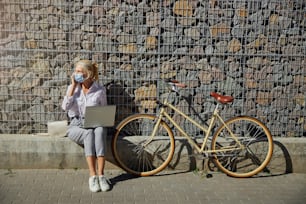 Fashionable female in white blouse and grey pants wit retro bike spending time in the city isolated on the stone wall