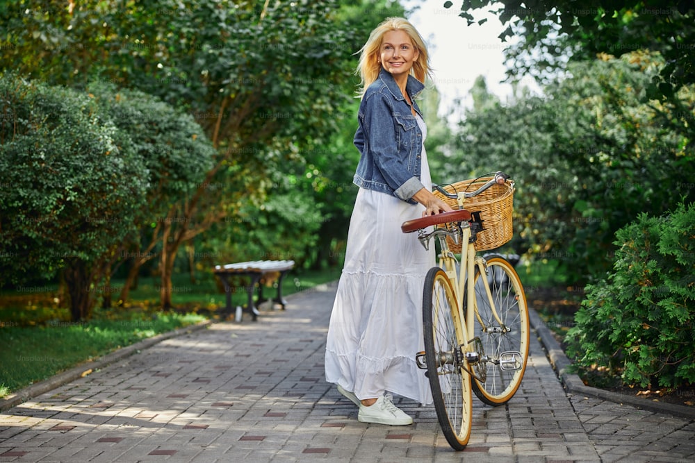 Retrato de la vista trasera de la mujer feliz y sonriente en vestido blanco que camina en el parque verde