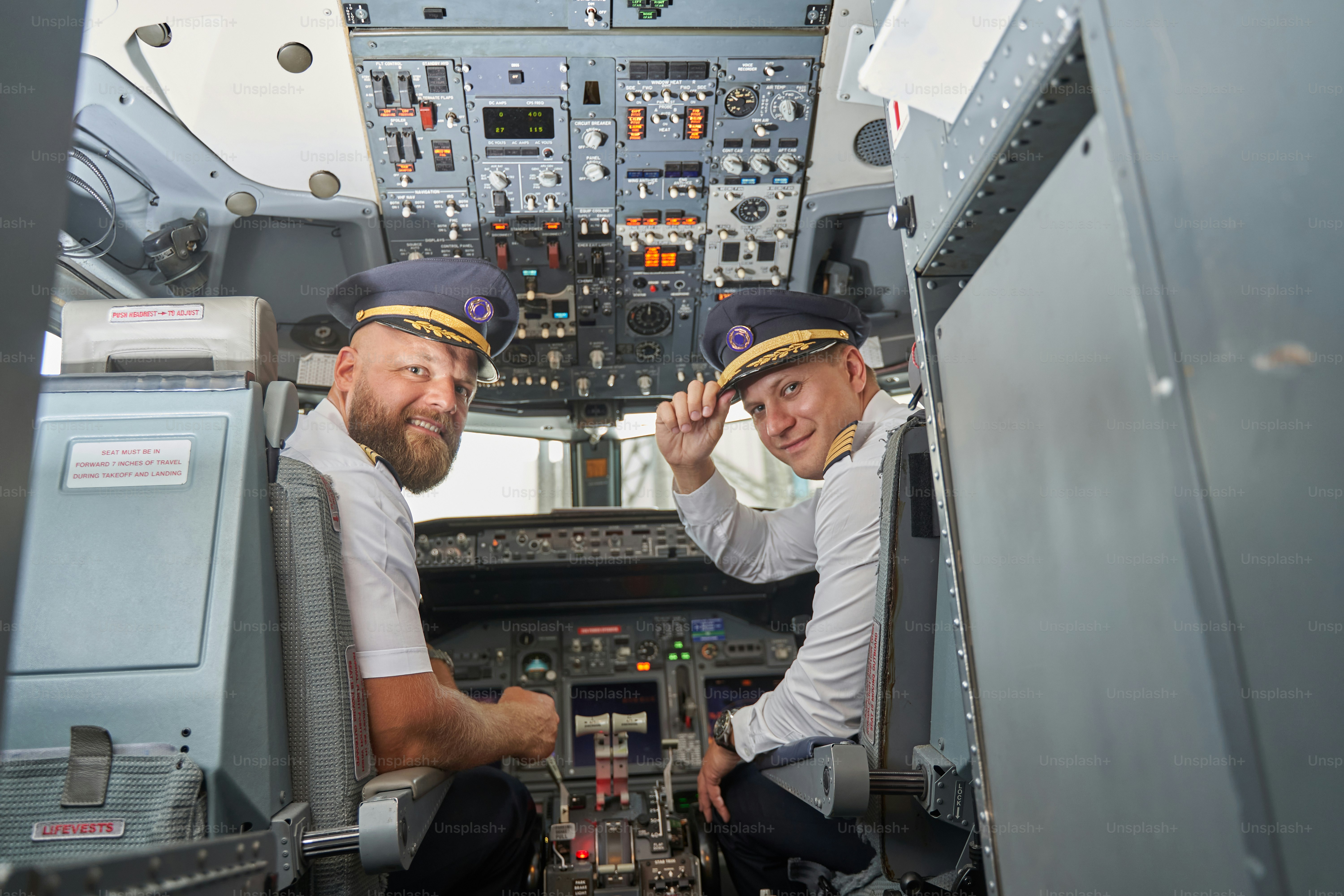 Contented professional airmen sitting in the control cabin of a modern aircraft and turning back with a smile