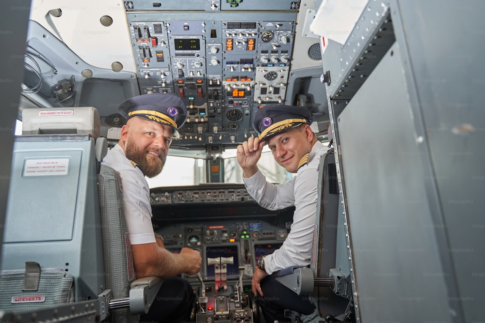 Aviadores profesionales satisfechos sentados en la cabina de control de un avión moderno y dándose la vuelta con una sonrisa