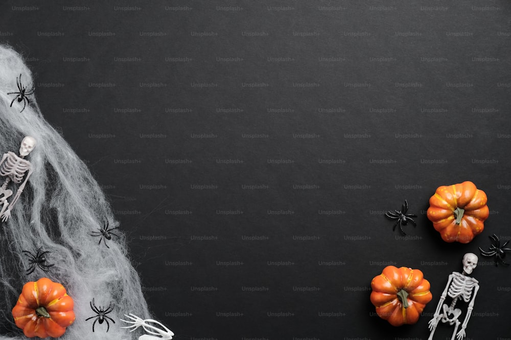 Mystery Halloween Hintergrund mit Kürbissen, Spinnweben, Skeletten, Spinnen auf schwarzem Tisch. Flaches Lay, Draufsicht, Kopierraum.