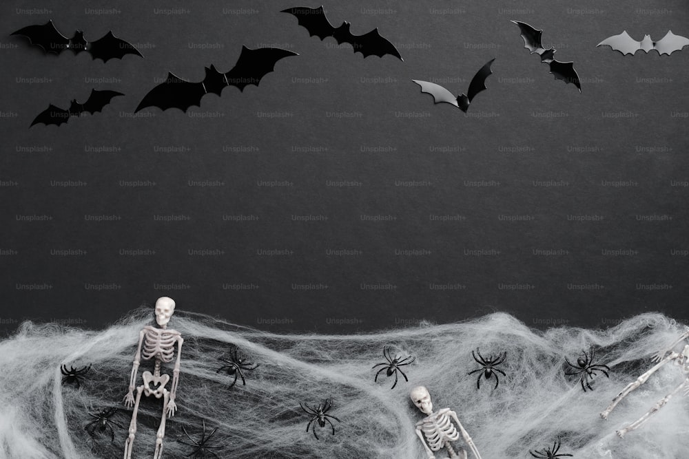 Carte de joyeux Halloween. Composition plate avec silhouette de chauves-souris, squelettes, araignées, toile d’araignée sur fond noir.