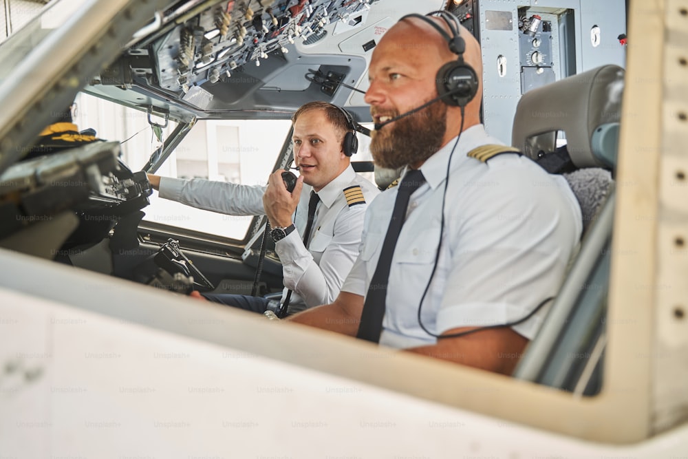 Aviadores alegres que usan auriculares del equipo de radio mientras están sentados en una cabina de vuelo y pilotan un avión