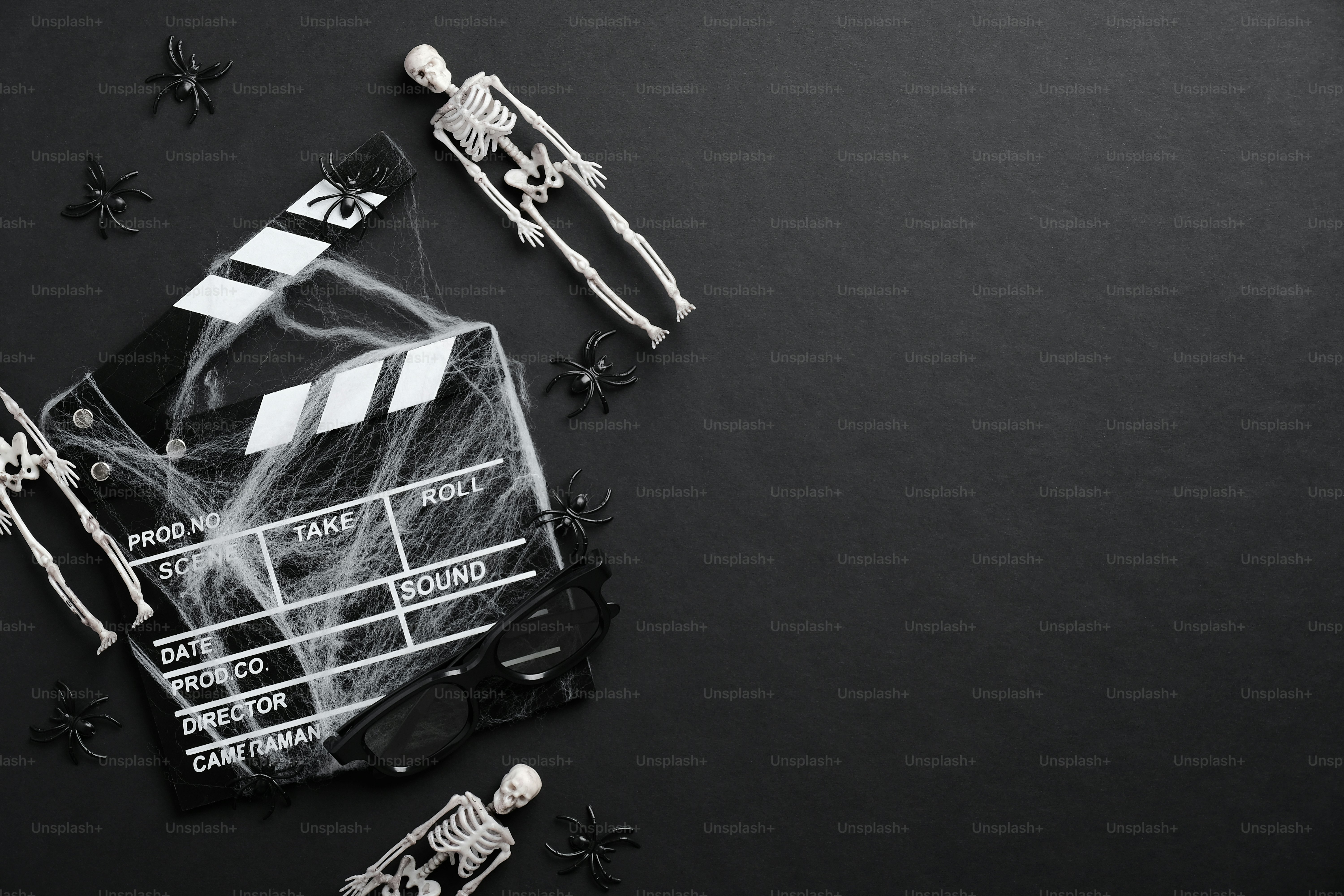 Halloween concept. Scary flat lay composition with movie clapper board in spider webs, skeletons on black background.