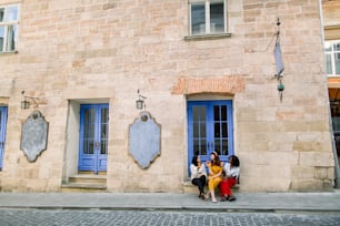 Tres jóvenes turistas multiétnicas, musulmanas, africanas y caucásicas, divirtiéndose en la calle en la vieja ciudad europea, sentadas en las escaleras bajo la puerta azul de la cafetería y comiendo croissants frescos.
