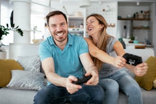 Husband and wife playing video game with joysticks in living room. Loving couple are playing video games at home