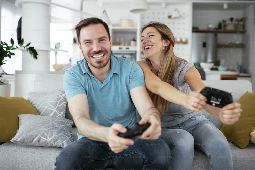 Husband and wife playing video game with joysticks in living room. Loving couple are playing video games at home