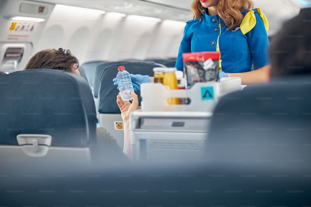 Cropped head portrait of flight attendant serving drinks to passengers on board commercial airplane