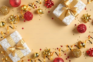 Christmas composition. Frame made of glittering Xmas decorations, gift boxes, red and golden balls, confetti on yellow background. Flat lay, top view. Season greeting card mockup.