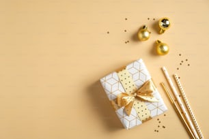 Christmas composition. Gift box, golden balls decorations, drinking straws on yellow background. Christmas party invitation card mockup