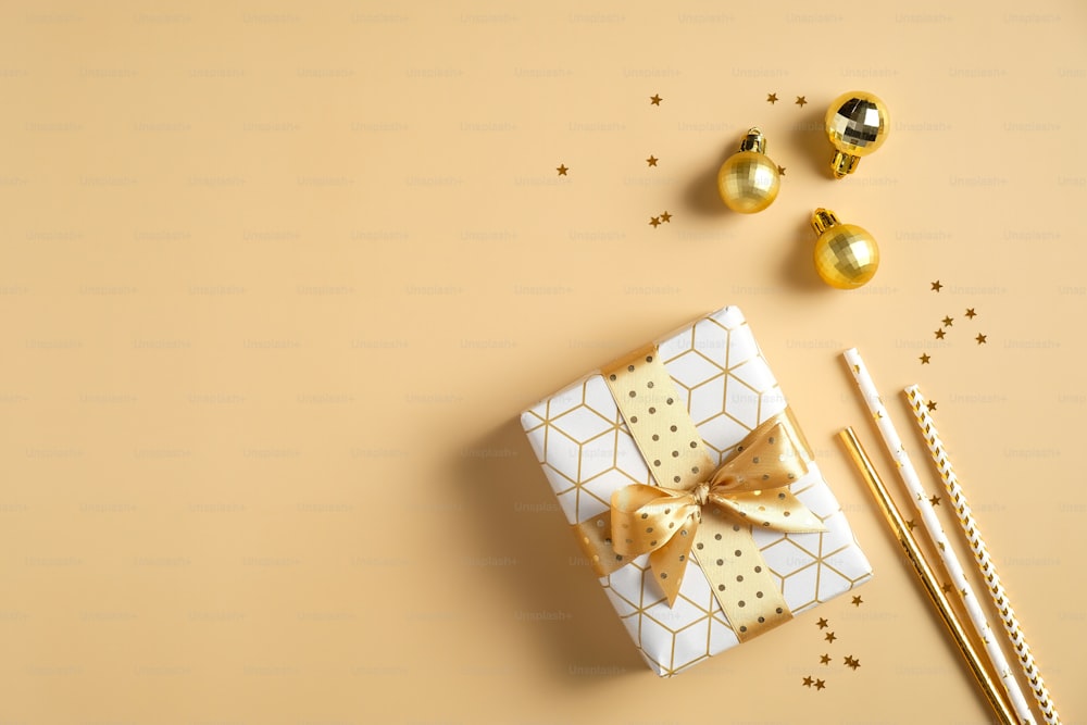 Composición navideña. Caja de regalo, decoraciones de bolas doradas, pajitas para beber sobre fondo amarillo. Maqueta de tarjeta de invitación a fiesta de Navidad