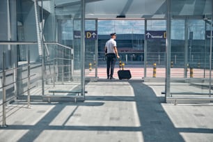 Trabalhador da companhia aérea com saco de bagagem de carrinho em pé pela porta de saída do terminal do aeroporto