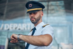 Jovem de boa aparência capitão da companhia aérea no chapéu de piloto verificando o tempo antes do voo no aeroporto